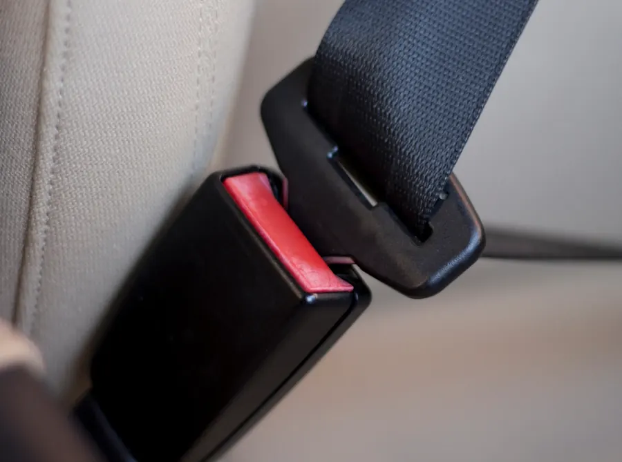 Seat belt tongue being guided towards the buckle receiver beside a vehicle seat