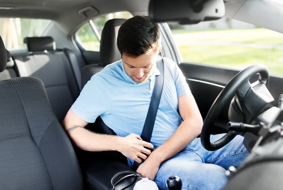 Driver seated with the seat belt fastened across the chest inside a vehicle cabin