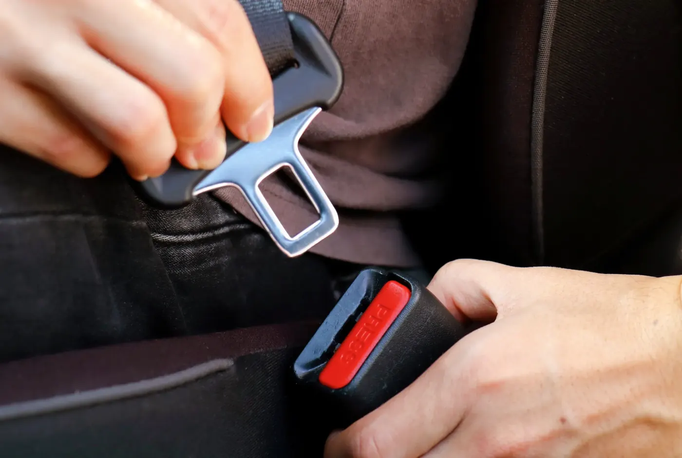 Hands guiding a seat belt latch plate towards the buckle receiver between vehicle seats