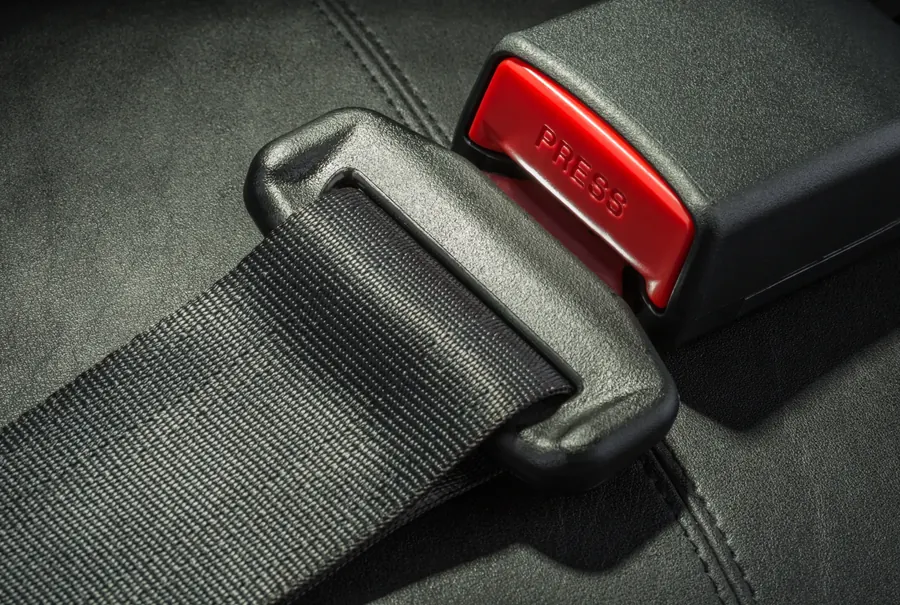 Seat belt webbing, latch plate and buckle receiver photographed close up on a dark seat