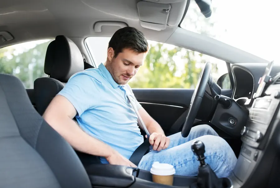 Driver in a passenger car reaching down to fasten the seat belt buckle beside the seat