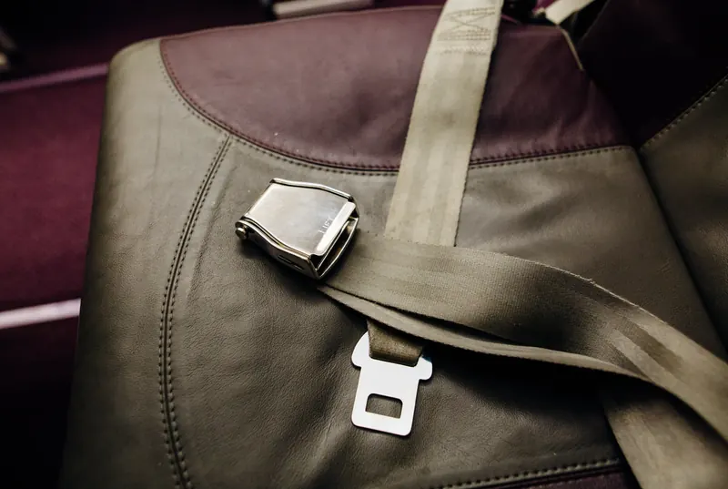 Metal lift-latch lap belt buckle resting on an olive coloured upholstered seat