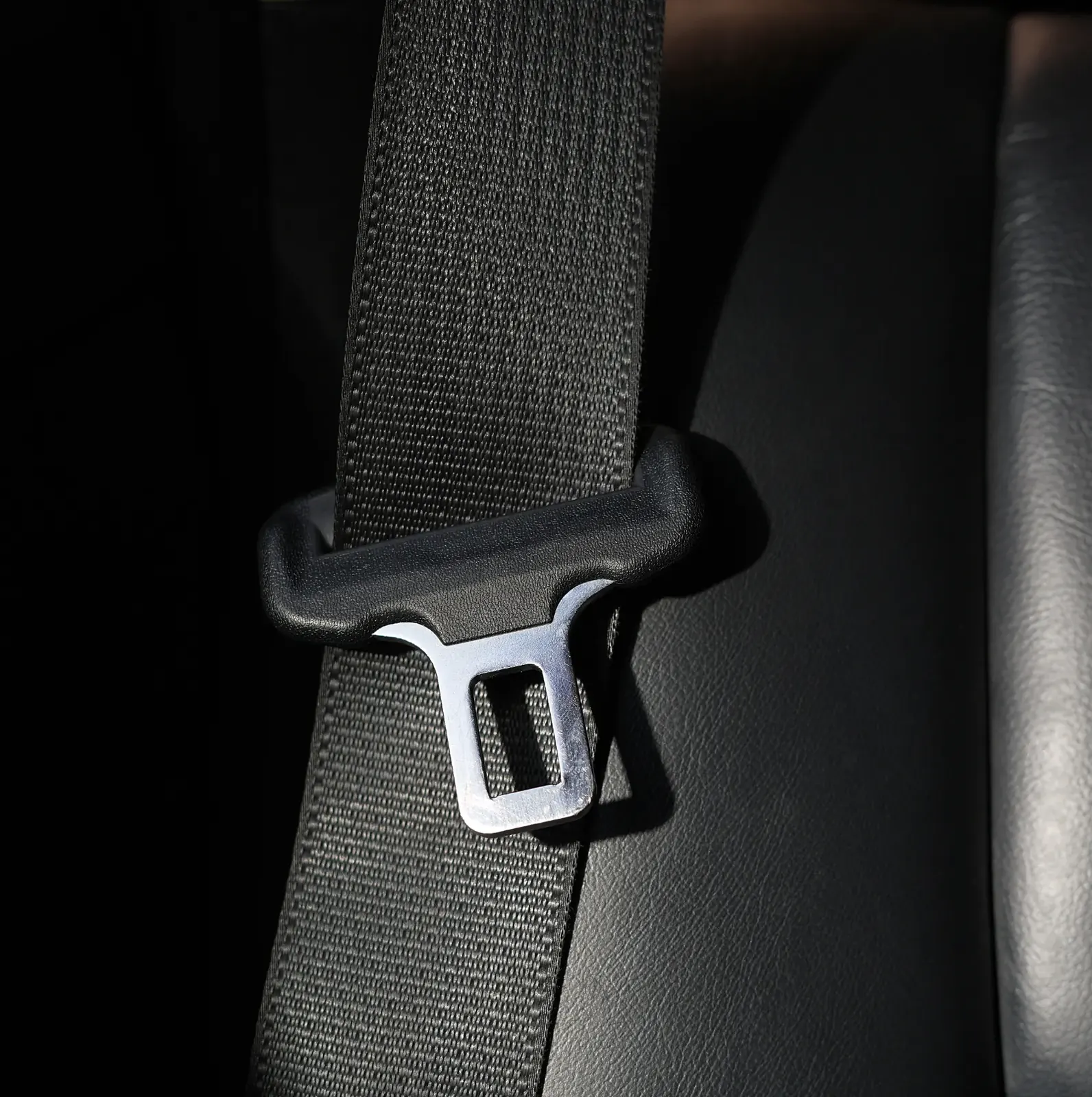 Seat belt webbing and metal latch plate photographed against a dark vehicle interior