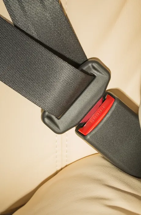 Seat belt webbing entering a buckle on a cream leather vehicle seat