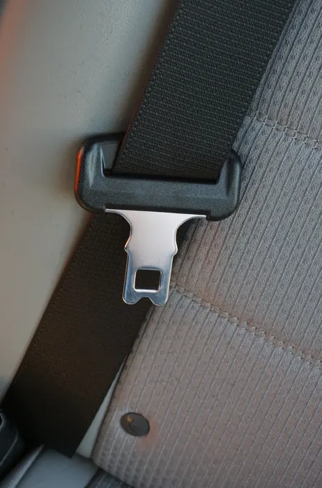 Metal seat belt latch plate resting against the webbing on a grey vehicle seat