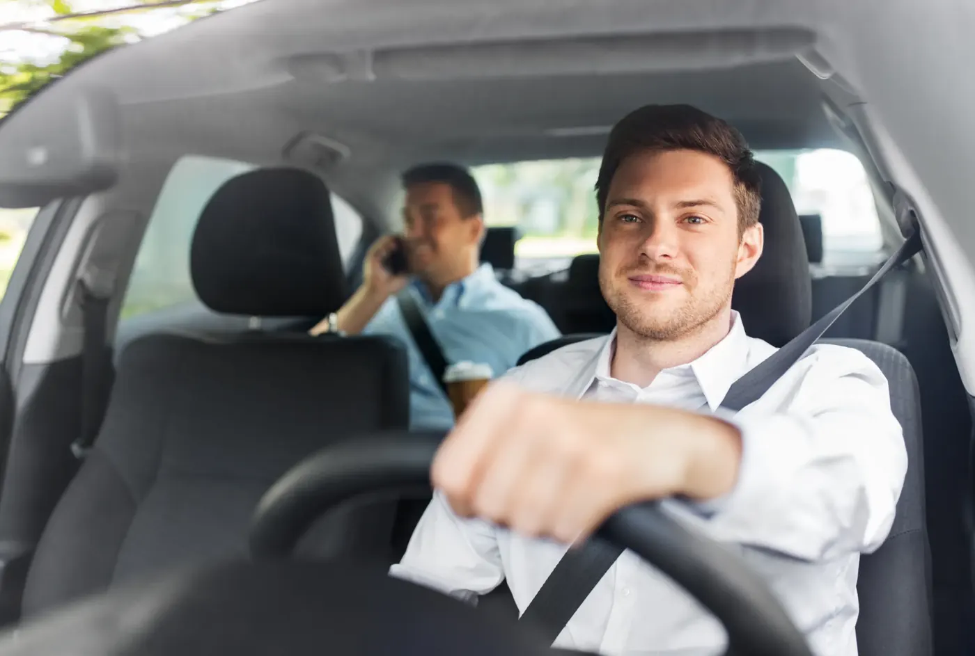 Driver and rear passenger travelling in a car, both wearing their seat belts across the shoulder