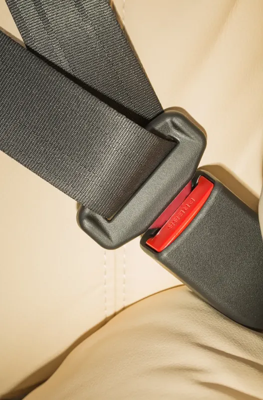 Seat belt webbing entering a buckle on a cream leather seat