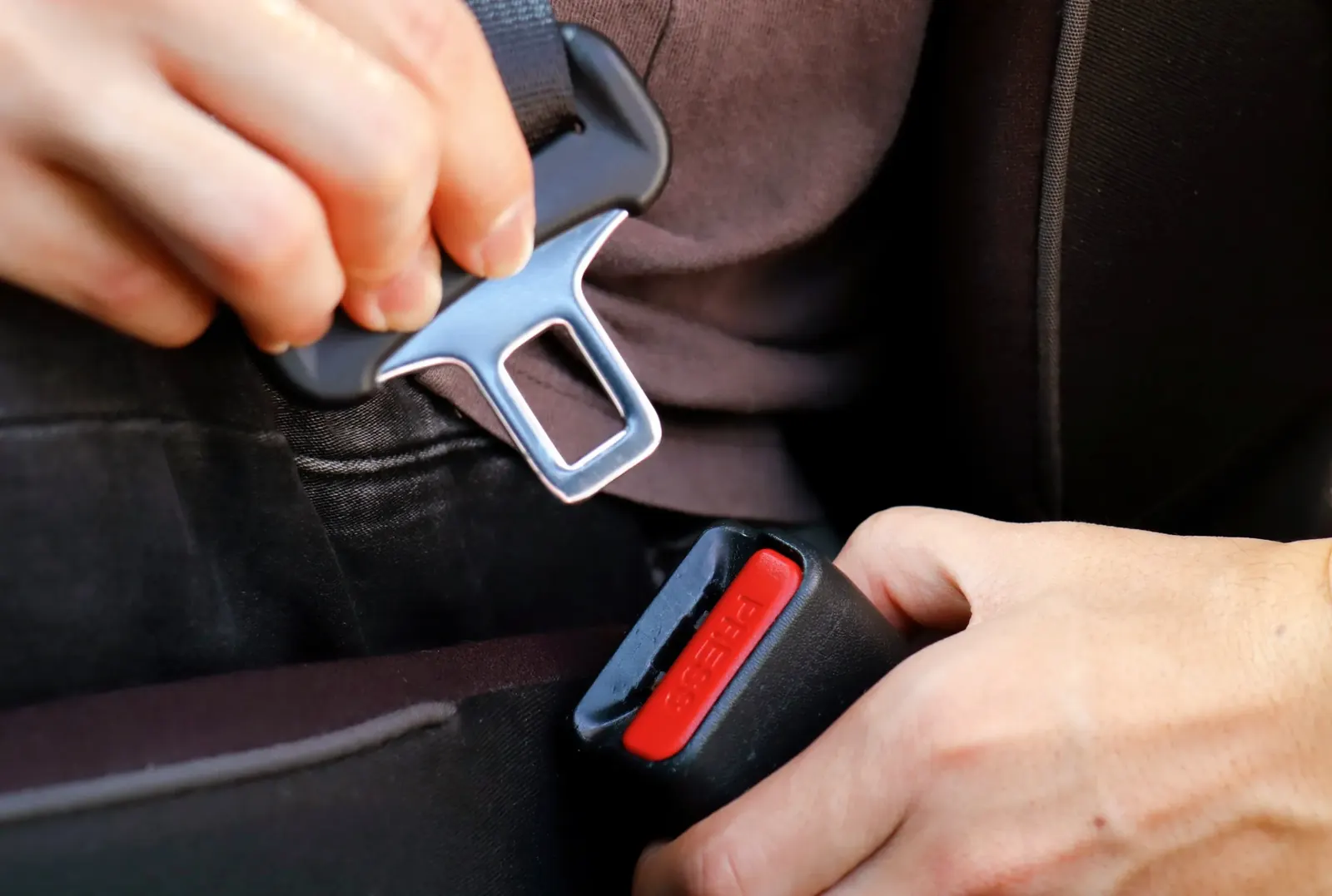 Hands guiding a seat belt latch plate towards the buckle receiver between two vehicle seats