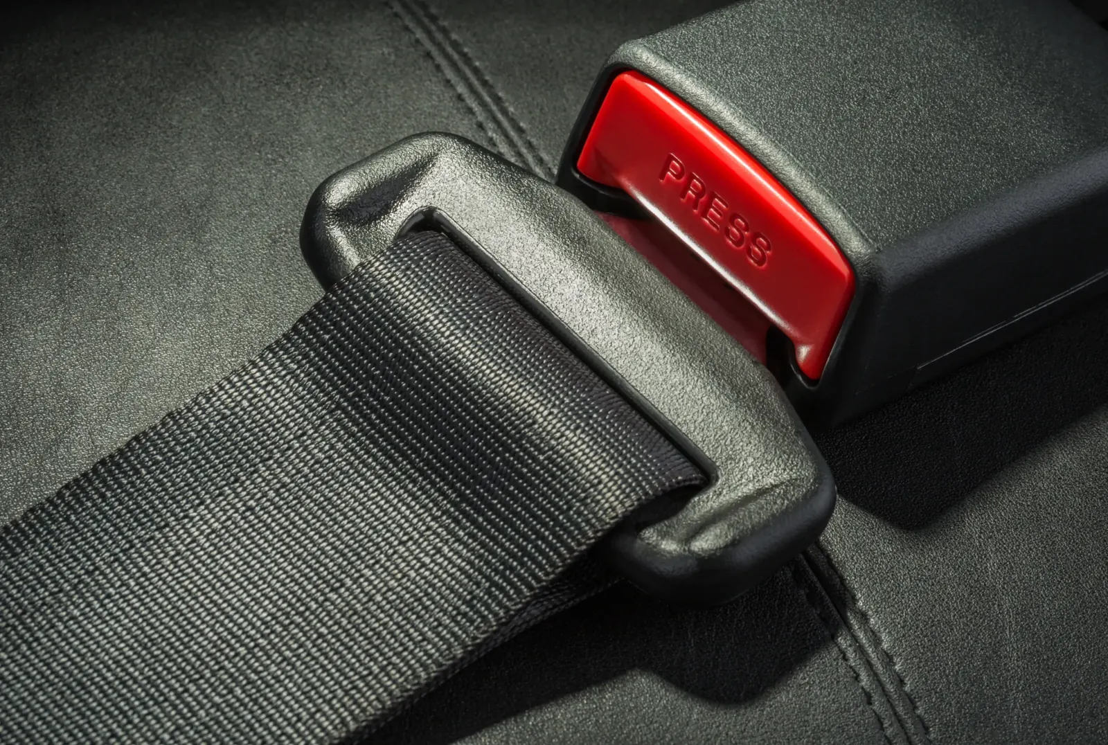 Macro view of seat belt webbing entering a latch plate beside a buckle receiver with a red release button